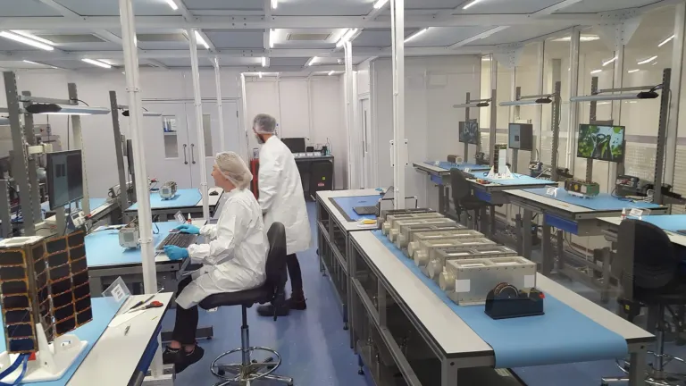 Staff in lab coats and hairnets working at benches in a cleanroom laboratory