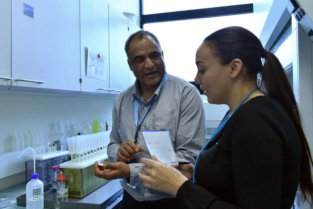 Two scientists in a laboratory discussing a printed results sheet